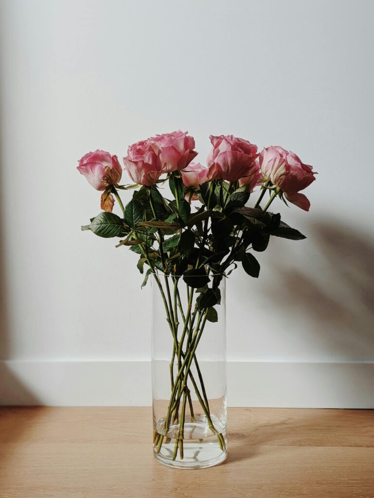 A beautiful arrangement of pink roses in a clear glass vase on a wooden surface indoors.